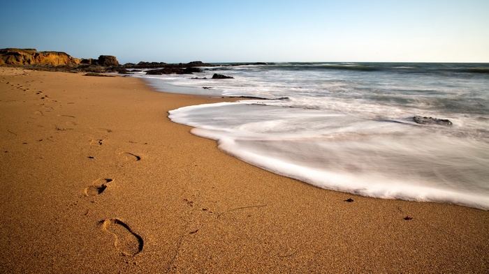 Footprints on a sandy beach with waves