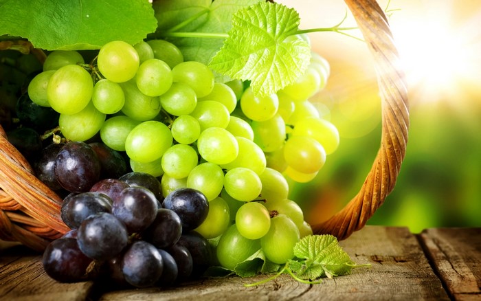 Basket of green and purple grapes on a wooden table