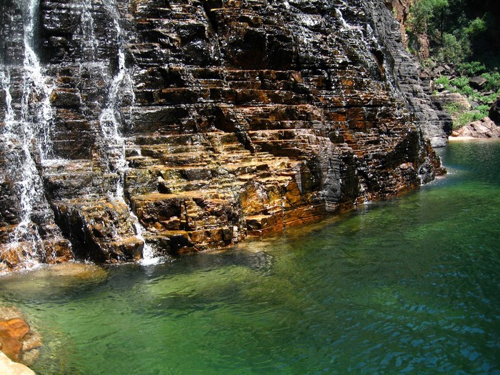 Waterfall cascading over layered rock into a clear green pool