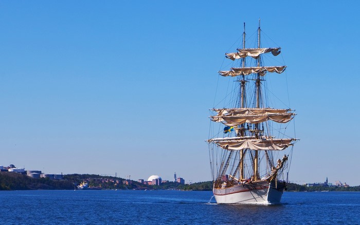 Tall ship sailing on blue water with city skyline