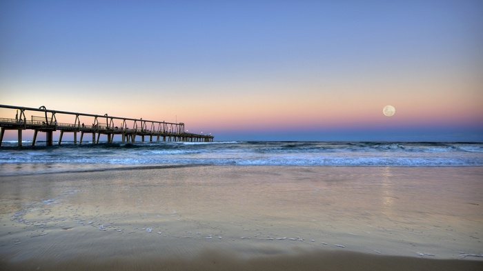 Pier and moon over ocean at sunset