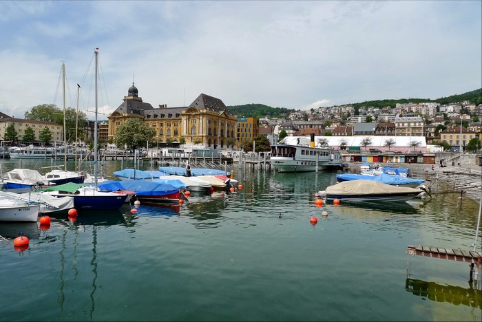 Boats docked in Neuchatel, Switzerland harbor with buildings in background