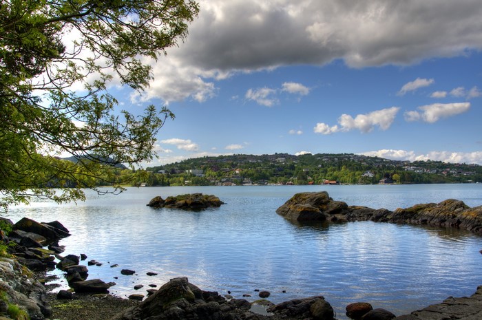 Rocky shore on a lake with forested hills and clouds