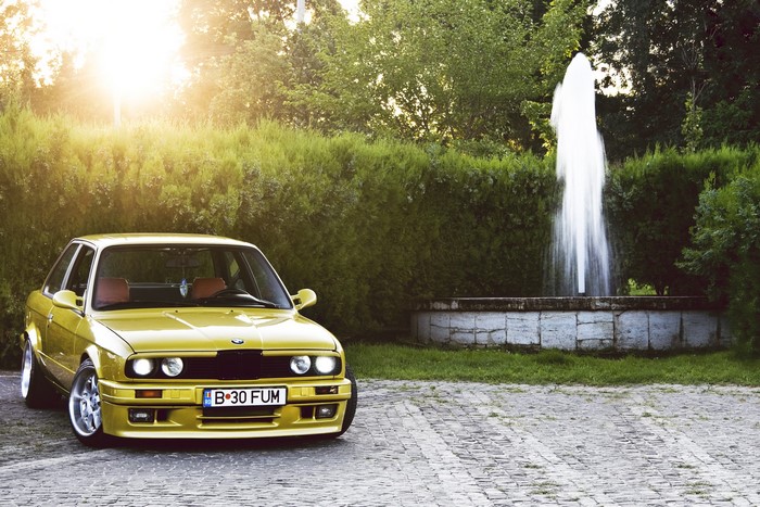 Yellow BMW E30 parked near a fountain
