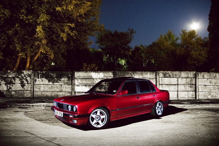 Red BMW E30 sedan parked at night