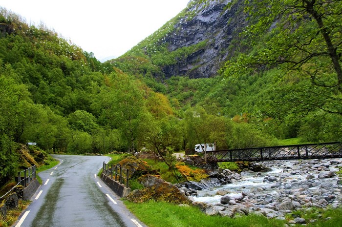 Road through a green mountain valley with a river and bridge