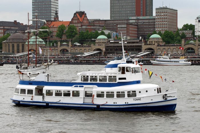 The passenger ship Tonne sails on the water with buildings in the background