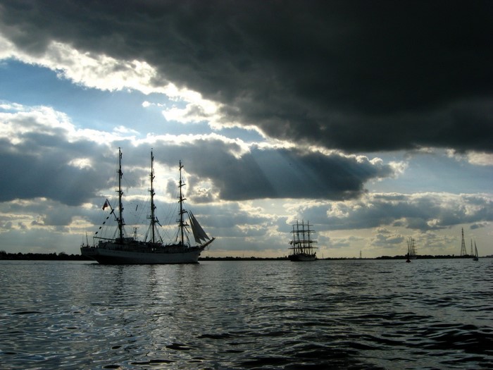 Tall ships sailing on the water under dramatic clouds