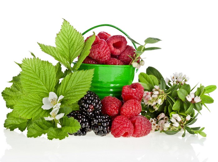 Raspberries and blackberries in a green bucket with leaves and flowers