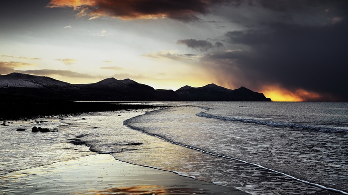 Stormy sunset over a rocky beach and mountains