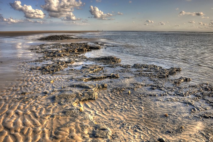 Rocky beach with rippled sand and ocean under cloudy sky