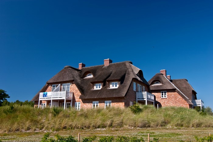 Thatched roof houses on a dune under a blue sky