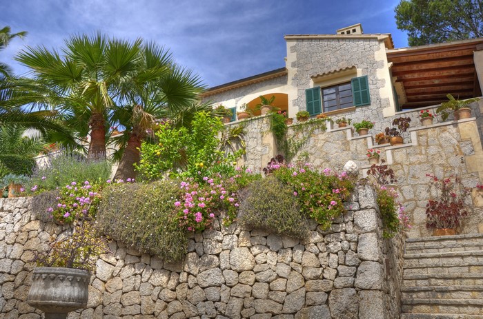Stone house with palm trees and flowers on a sunny day