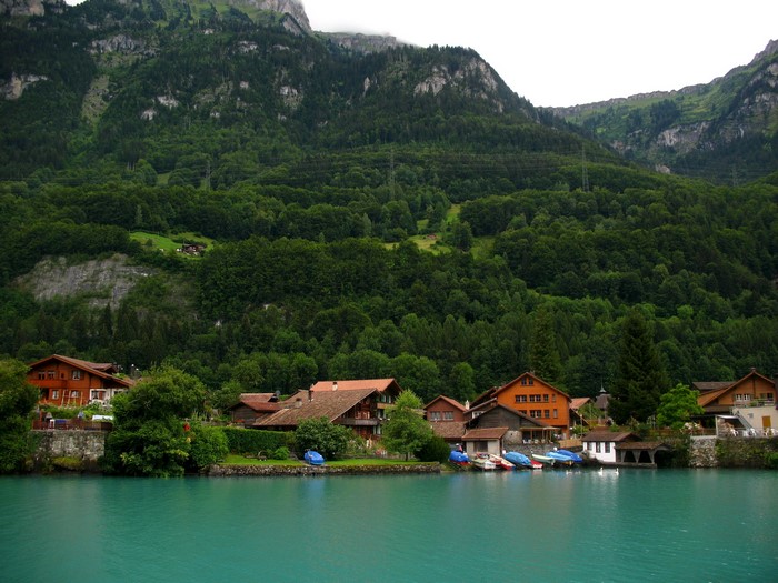 Houses on the shore of a turquoise lake with mountains in the background