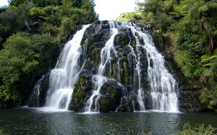 A wide waterfall cascades over moss-covered rocks into a pool below.