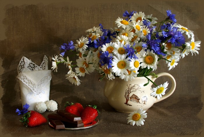 Bouquet of daisies and cornflowers in a jug with strawberries and chocolate