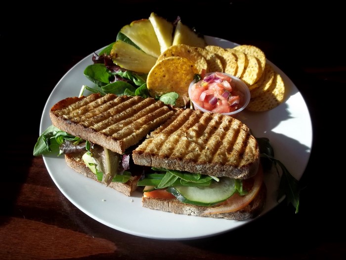 Grilled sandwich with salad, chips, and pineapple