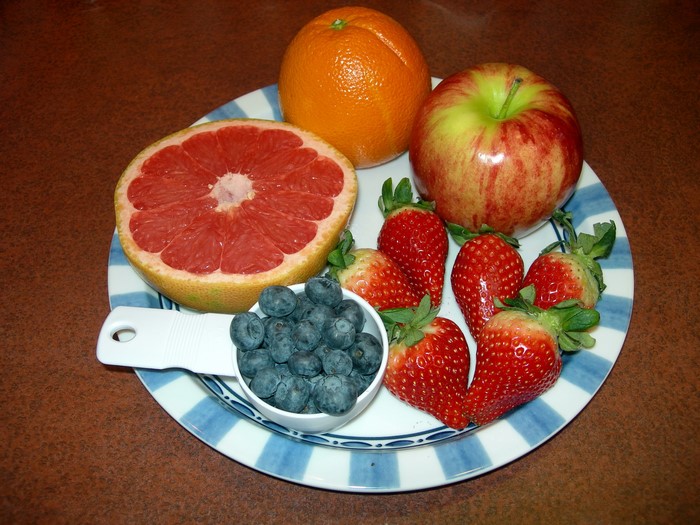 Plate of assorted fruits including grapefruit, orange, apple, strawberries, and blueberries