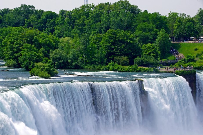 Niagara Falls with lush green trees and people on viewing platforms