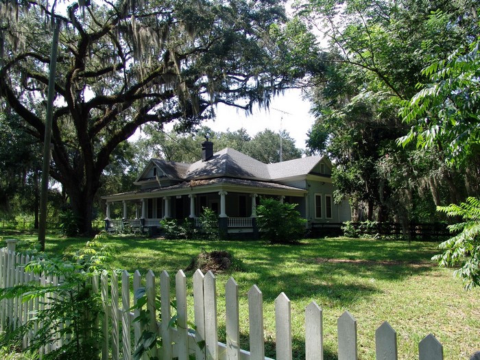 Old house in Florida surrounded by trees and a white picket fence