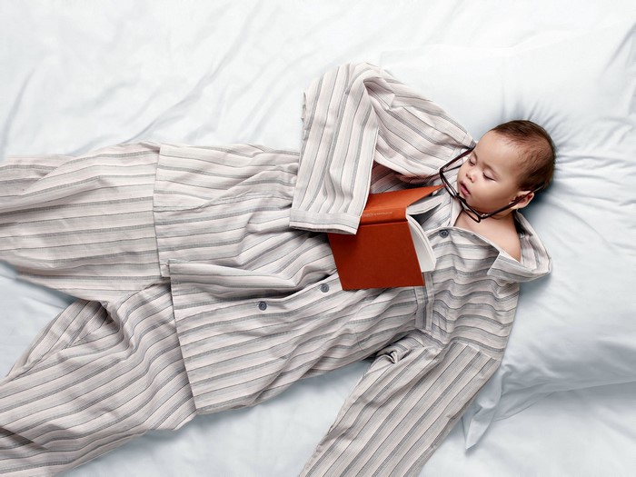 Baby in oversized pajamas sleeping with a book and glasses