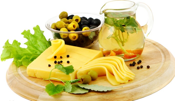 Cheese, olives, and dressing on a wooden board