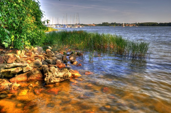 Boats docked on a river with rocky shore and green foliage