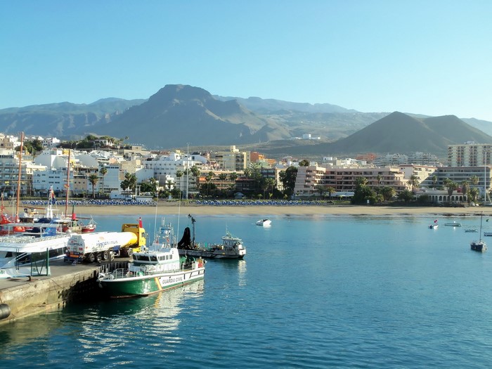 Boats docked in a harbor with a coastal town and mountains in the background, Spain