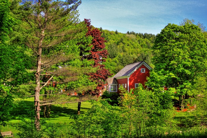 Red house nestled among green trees and hills