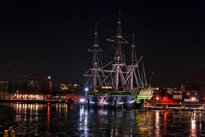 Tall ship docked at night with city lights and reflections