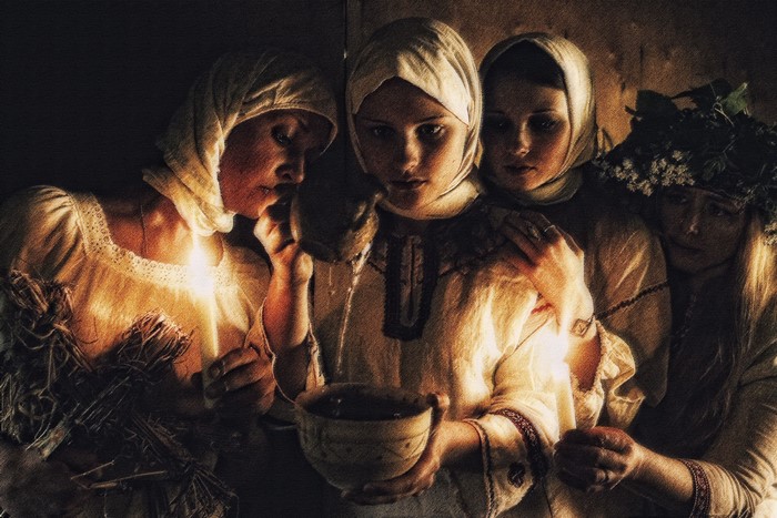 Four women in traditional clothing holding candles and a bowl
