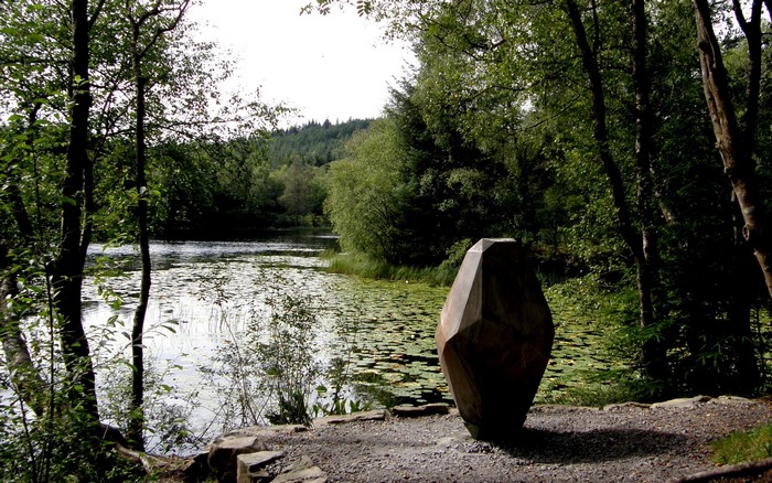 Sculpture by a lake with lily pads and trees