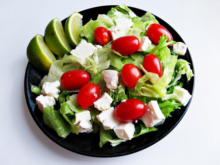 Salad with feta cheese, cherry tomatoes, and lime wedges