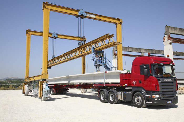 Scania truck transporting a concrete beam under a gantry crane