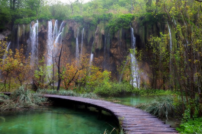 Wooden walkway through a park with waterfalls