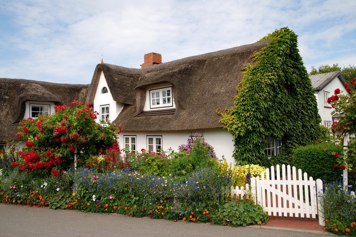Thatched roof house with garden and white picket fence