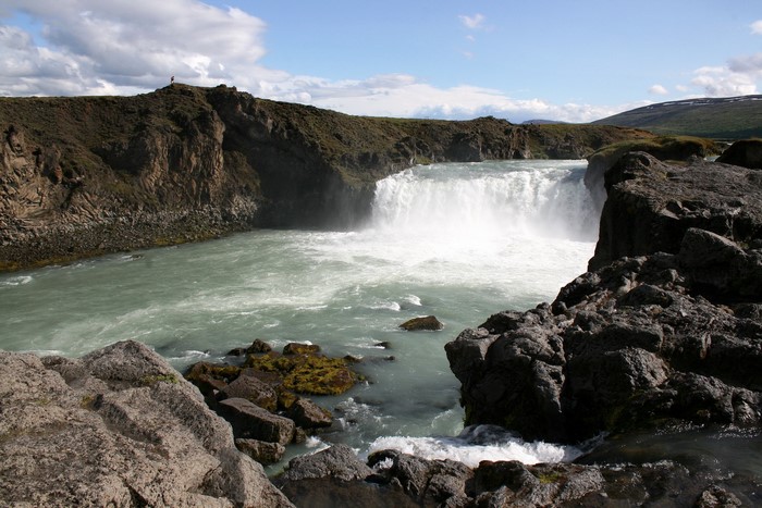 Waterfall cascading into a turquoise river with rocky shores