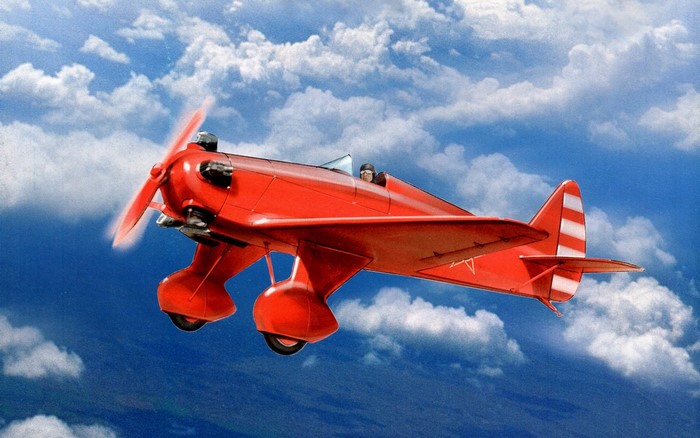 Red biplane flying in a blue sky with clouds