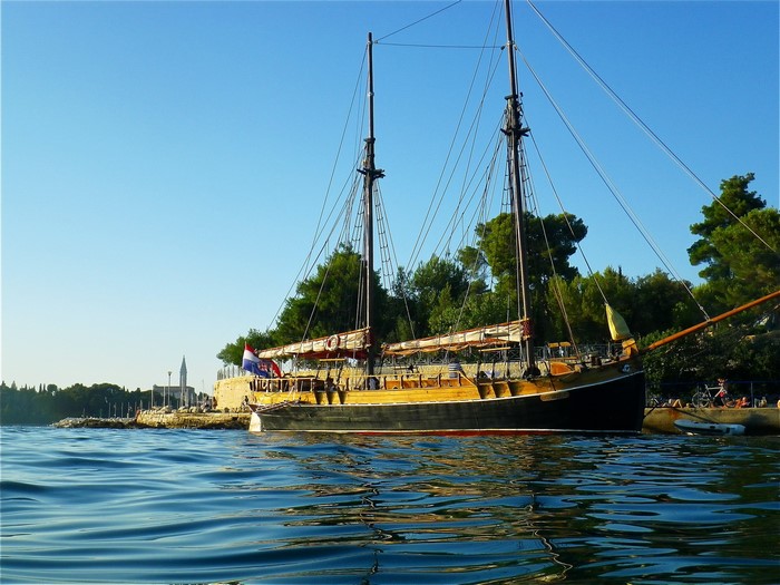 Wooden sailing ship docked by a stone pier with trees