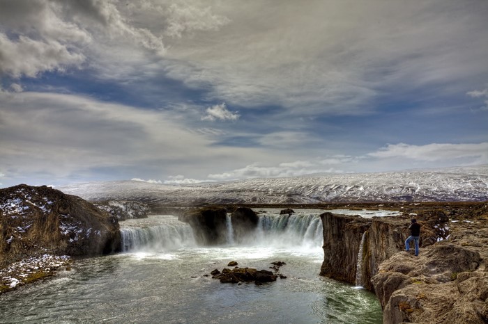 Man standing on cliff edge overlooking a waterfall