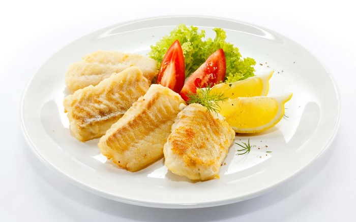 Fried fish fillets with lemon and salad on a plate