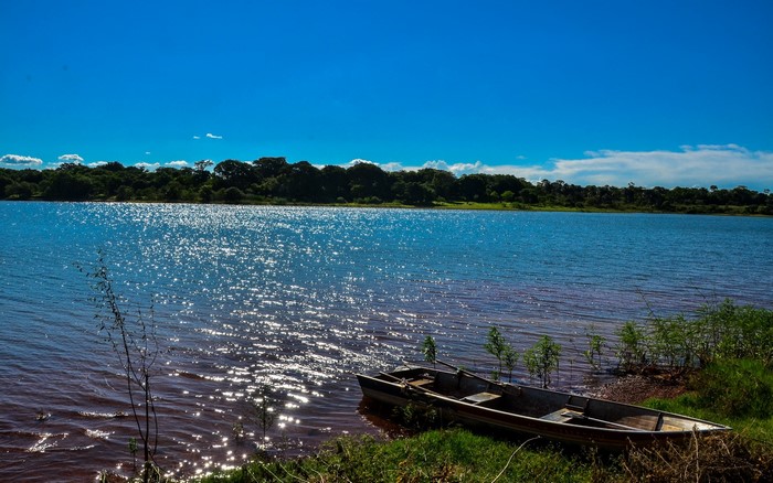 Boat on the shore of a wide river under a blue sky