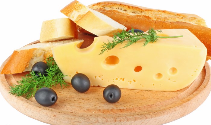 Cheese, bread, olives, and dill on a wooden board