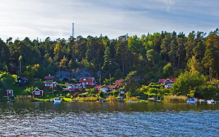 Red houses on a forested hillside by the water in Sweden