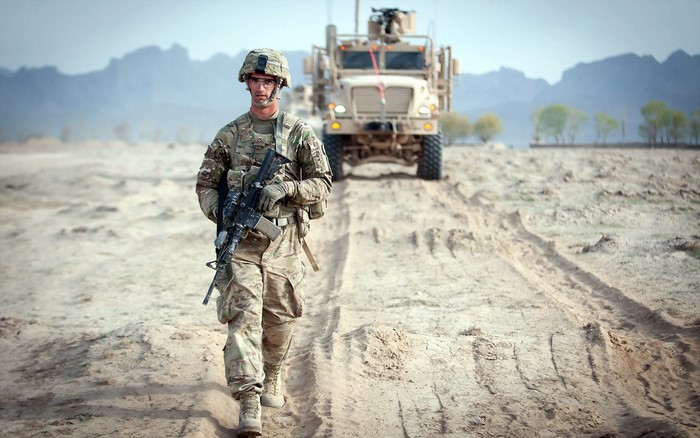 Soldier walking in desert with military vehicle