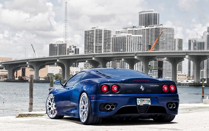 Blue Ferrari 360 Modena parked by water with city skyline