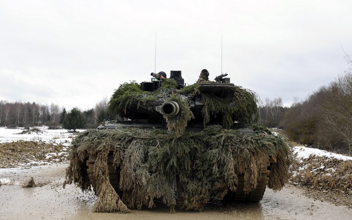 Camouflaged tank with soldiers in a muddy field