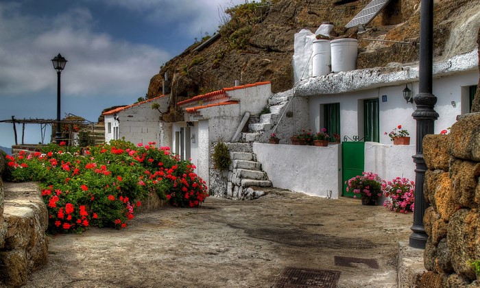 White houses built into a rocky hillside with red flowers in Spain
