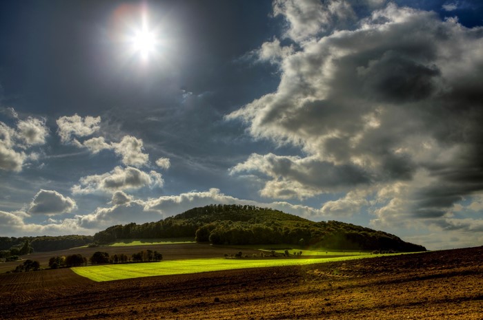 Sunlit fields and rolling hills under cloudy sky