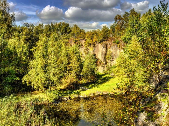 Quarry lake with trees and rocky cliffs under clouds